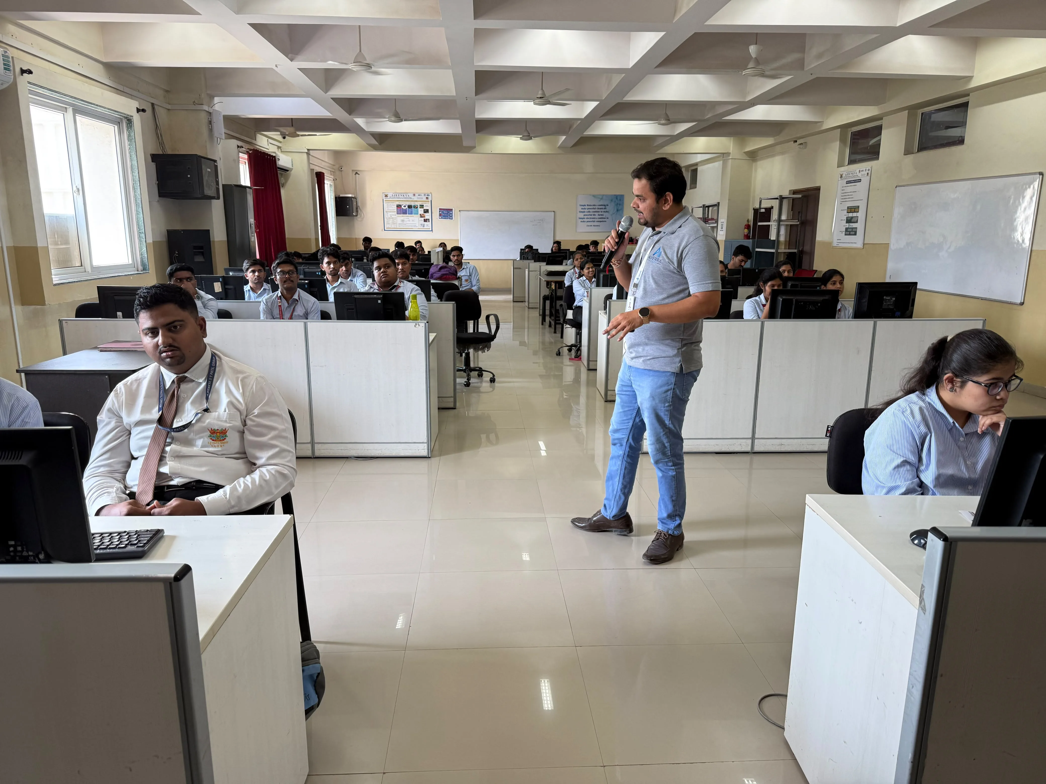 A trainer speaking to students seated at computers in a large college computer lab