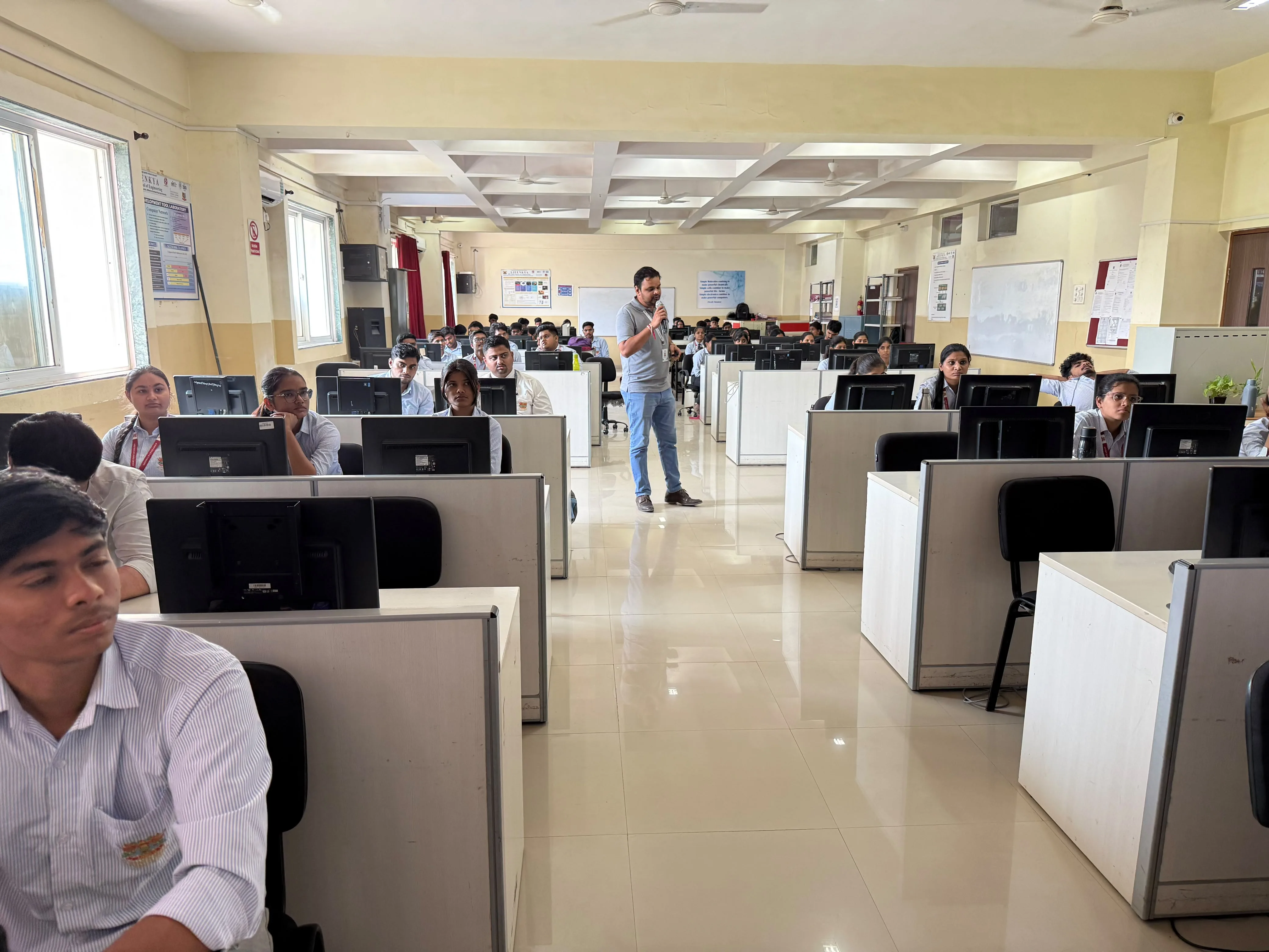 A trainer addressing rows of students at computers in a bright computer lab